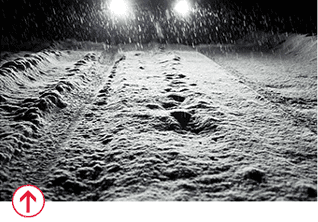 Car driving in winter weather in the dark with headlights on